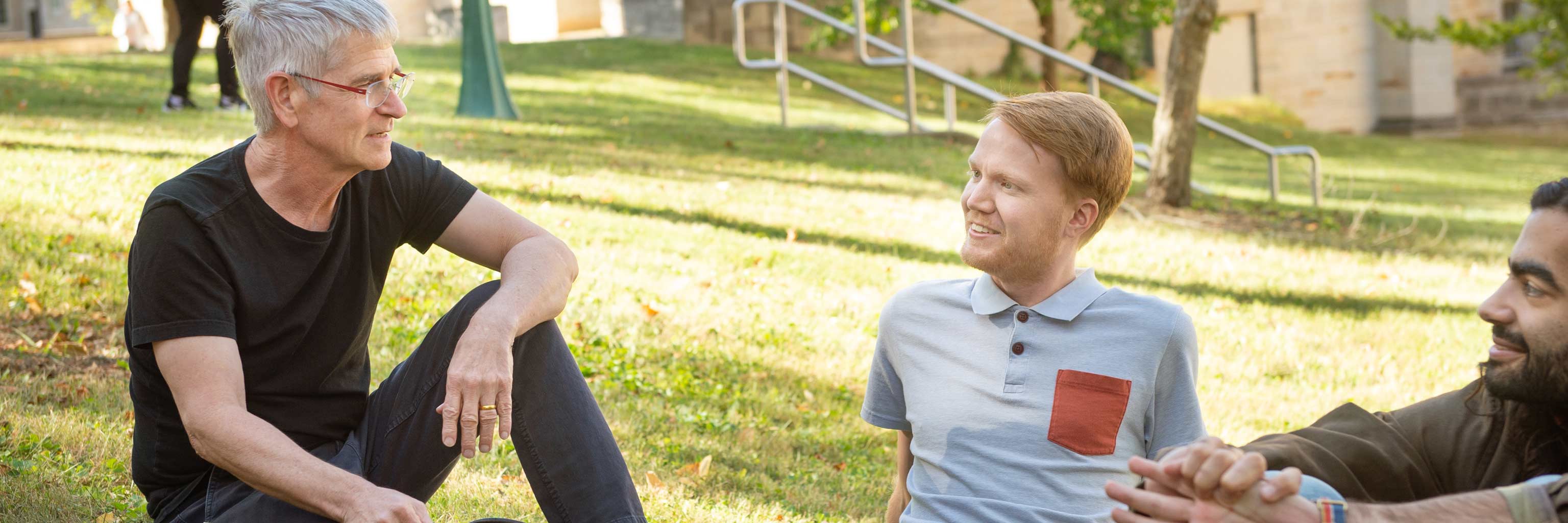 Students and a professor having a conversation as they sit outside.