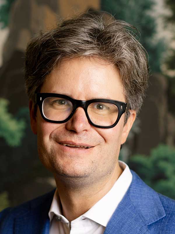 A headshot of Matthew Adams, who wears a blue blazer and white dress shirt.