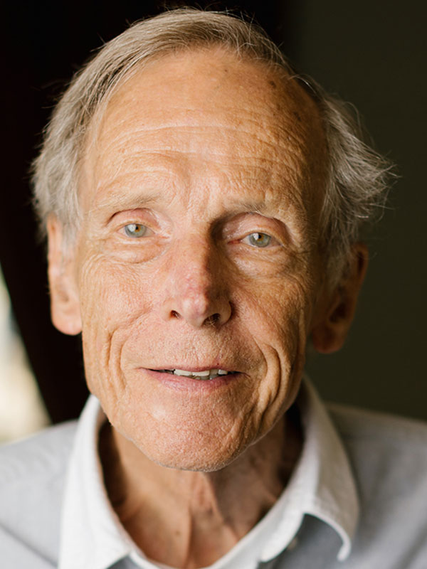 A headshot of Milton Fisk, who wears a white collared shirt and poses against a black background.