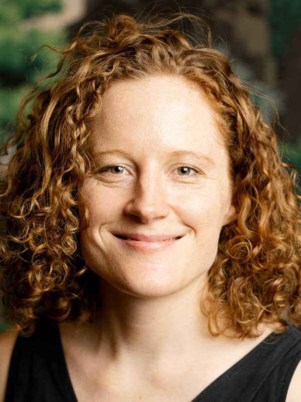 A headshot of Vera Flocke, who wears a black shirt and poses against a green background.