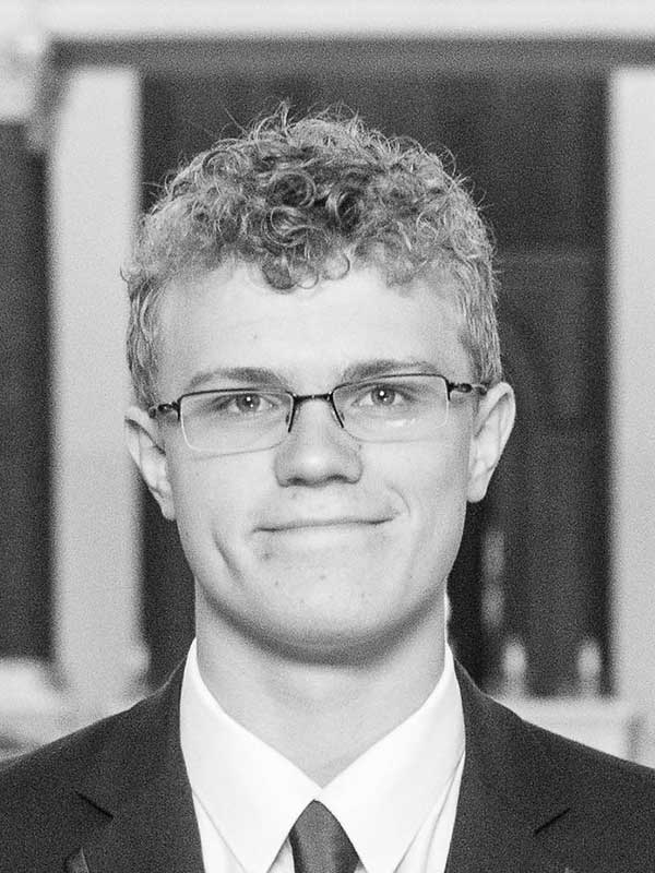 A black-and-white headshot of Adam Lawal, who wears a dark suit and tie.