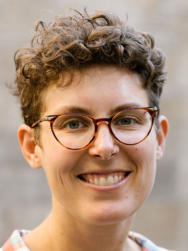 A headshot of Katy Meadows, who wears a red and white flannel shirt and poses in front of a blurry beige background.