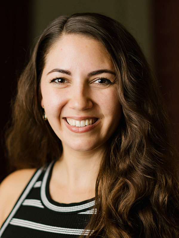 A headshot of Savannah Pearlman, who wears a black and white striped shirt and poses against a dark background.