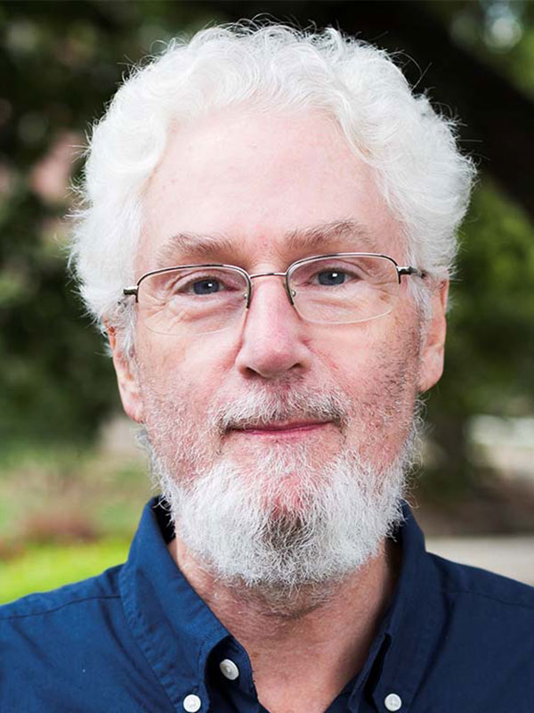 A headshot of Fred Schmitt, who wears a dark blue dress shirt and poses outside.