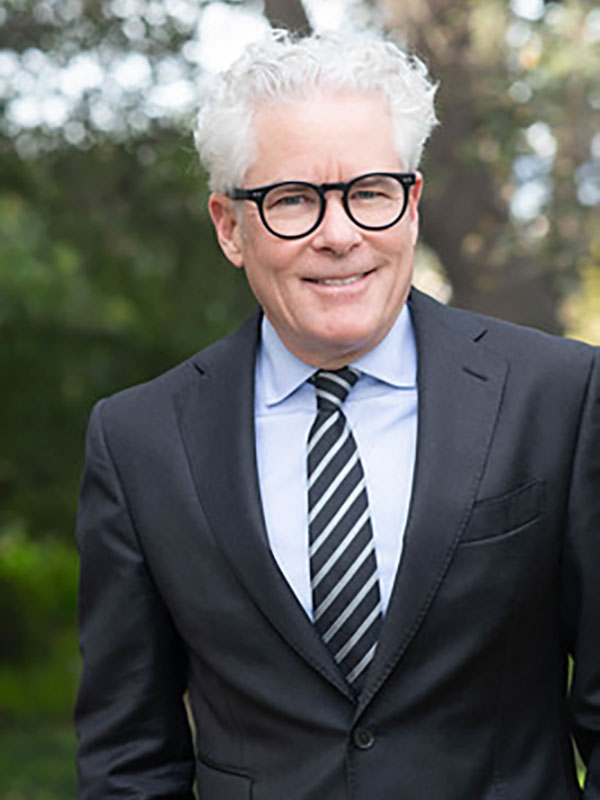 A photo of R. Jay Wallace, who wears a black suit and a blue dress shirt, and poses outside.