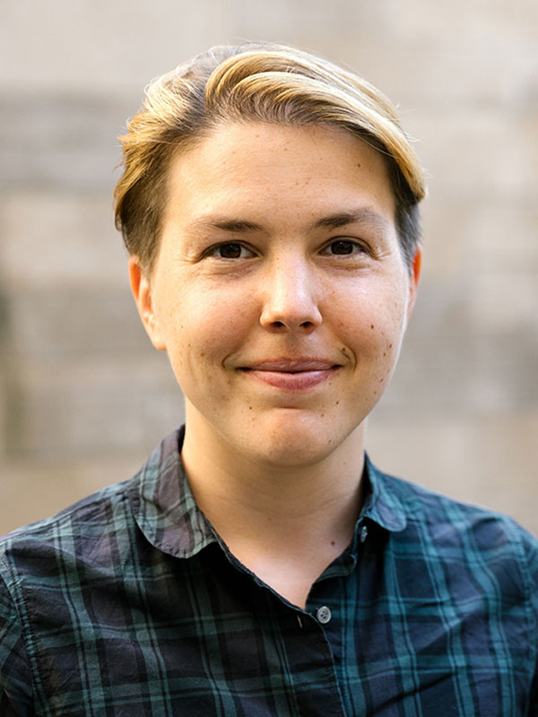 A headshot of Elizabeth Williams, who wears a green and black striped dress shirt and poses against a blurry beige background.